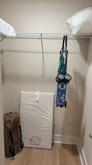 Eine Ecke eines Zimmers mit einem weißen Matratze, einer blauen Matratze auf einem Gestell, einer weißen Tasche und einem an der Wand befestigten Rack mit einem grünen Gegenstand.