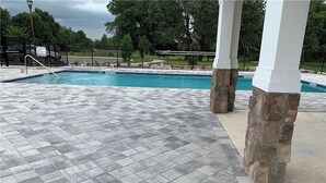Una piscina con suelo de baldosas a cuadros, pilares de piedra y una valla al fondo.