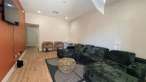 Ein Wohnzimmer mit einer Couch, zwei Sesseln, einem kleinen Tisch und einem an der Wand befestigten Fernseher.