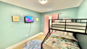 Une chambre avec un lit superposé, une télévision, un petit tapis rond et une fenêtre avec des rideaux.