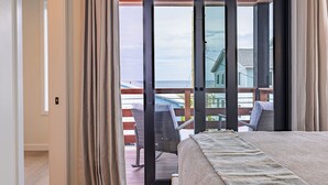Ein Schlafzimmer mit einem großen Fenster, einem Bett und Blick auf einen Balkon mit Stühlen.