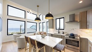Eine moderne Küche mit einer großen Kochinsel, Edelstahlgeräten und Blick auf den Ozean.