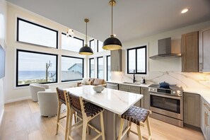 Eine moderne Küche mit einer großen Kochinsel, Edelstahlgeräten und Blick auf den Ozean.
