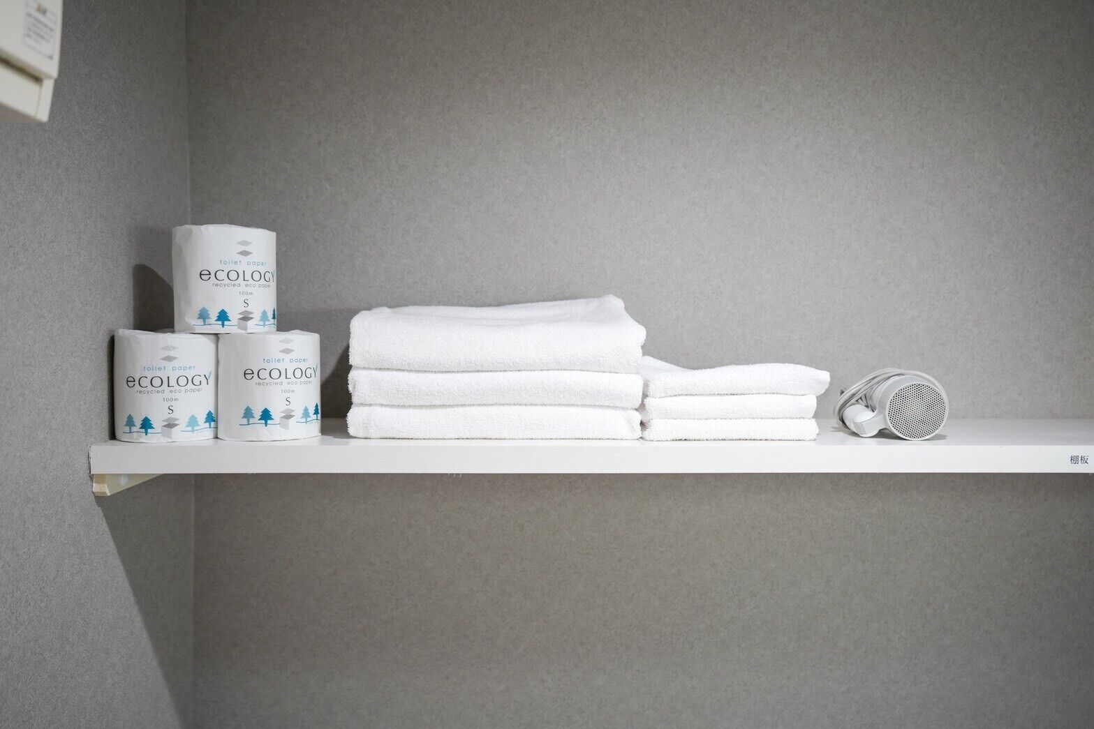 A bathroom shelf with toilet paper, towels, and a shower head.