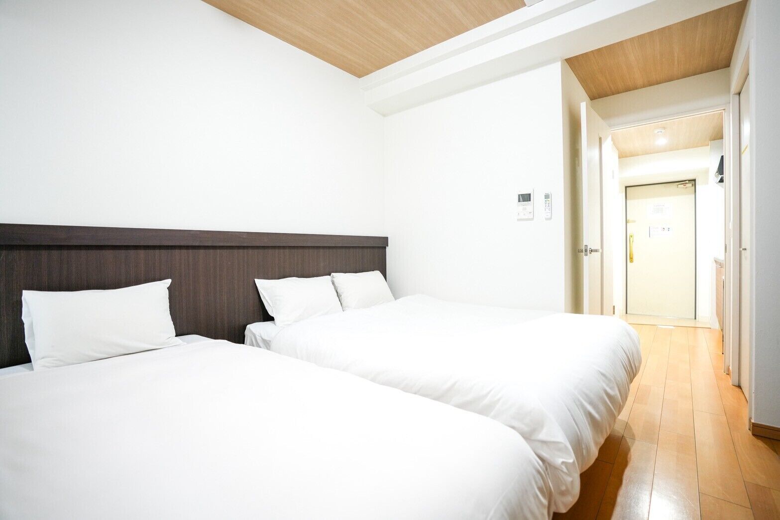 A hotel room with two beds, a wooden ceiling, and a door leading to a hallway.