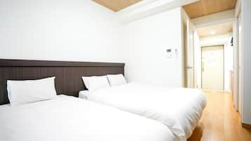 A hotel room with two beds, a wooden ceiling, and a door leading to a hallway.