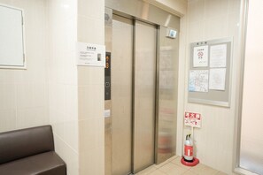 Ein Aufzug mit digitaler Anzeige, einem Feuerlöscher und Informationstafeln in der Hotelhalle.