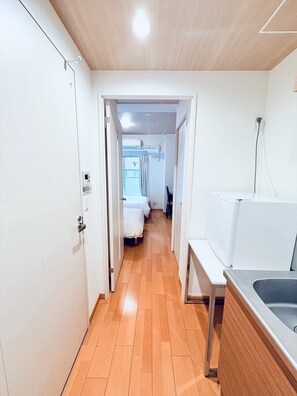 A narrow hallway with wooden flooring, white walls, and a visible bed in the distance. - HOTEL J&C-I (Osaka city)