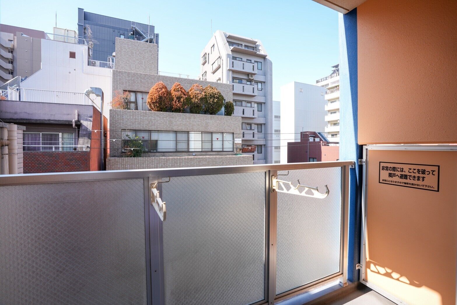 A view from a balcony with a metal railing, a building with a modern design, and a sign with Japanese text.