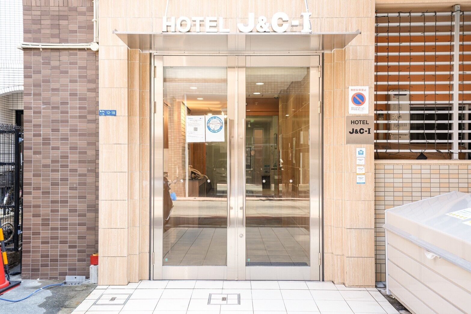 The entrance to HOTEL J&C-I with a tiled facade, a glass door, and a sign indicating no parking.