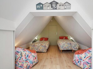 Un dormitorio tipo desván con dos camas, suelo de madera y techo inclinado.