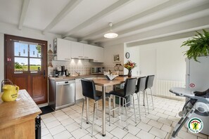 A kitchen with a wooden table, black chairs, a coffee machine, and a dishwasher. - Gîtes de France® - Gîte des Nénuphars (SAINT JOUIN BRUNEVAL)