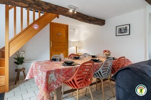 A dining area with a wooden staircase, a table set for four, and a framed picture on the wall. - Gîtes de France® - Gîte des Nénuphars (SAINT JOUIN BRUNEVAL)