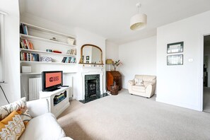 A living room with a fireplace, a sofa, a television, and a bookshelf. - GuestReady - Modern Retreat with Classic Charm (London)