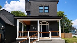 Een tweelaags huis met een donkere buitenkant, een veranda met houten leuningen en een groot rondboogvenster.