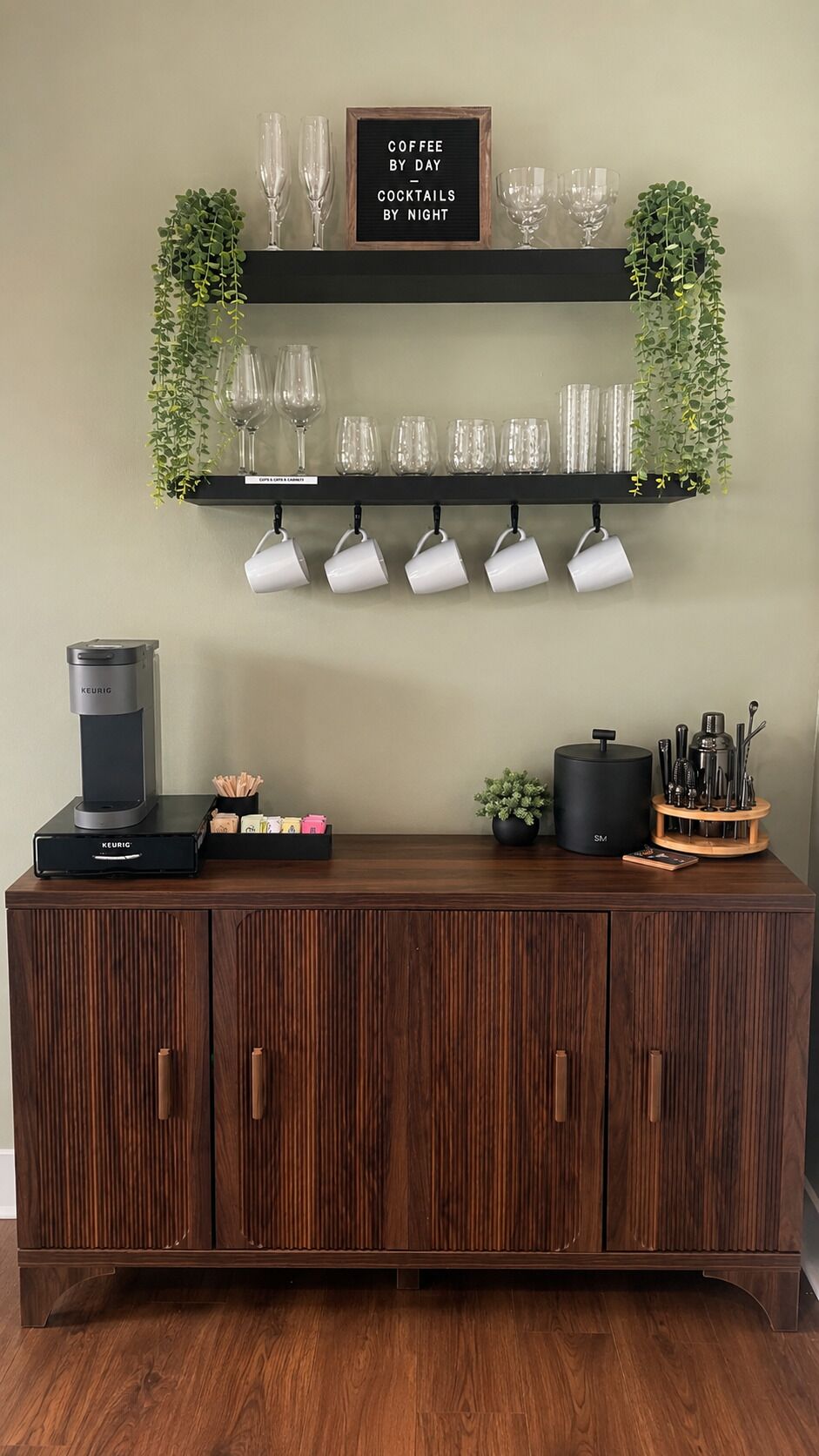 Un mueble de madera con cafetera, tazas y un cartel que dice 'Café durante el día, cócteles por la noche'.