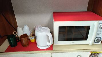 Un horno microondas con parte superior roja, una cafetera blanca, una taza verde y una taza amarilla sobre un tapete rojo dentro de un gabinete de madera.