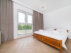 A bedroom with a large window, a wooden bed, and a white wall.