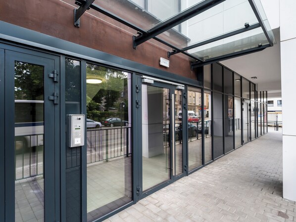 A modern building entrance with glass doors, a metal frame, and a paved walkway.