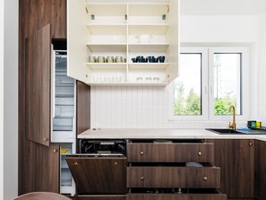 A modern kitchen with wooden cabinets, a built-in dishwasher, and a window with a view of greenery.
