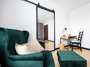 A room with a green sofa, a desk with a chair, and a large mirror. - Targowa Elegant Apartment (Łódź)