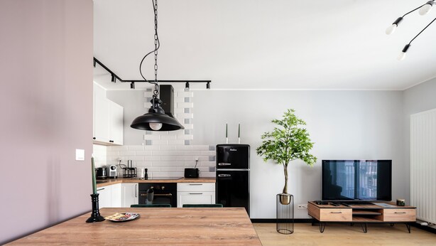 Una cocina moderna con armarios blancos, un refrigerador negro y un comedor con mesa de madera y sillas verdes.