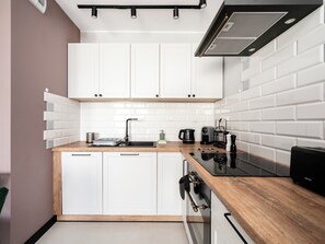 A modern kitchen with white cabinets, a wooden countertop, a black stove, and a coffee maker. - Targowa Elegant Apartment (Łódź)