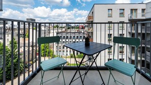 Un balcón con mesa y sillas, con vistas a un paisaje urbano con edificios y cielo despejado.