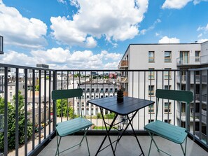 A balcony with a table and chairs, overlooking a cityscape with buildings and a clear sky. - Targowa Elegant Apartment (Łódź)