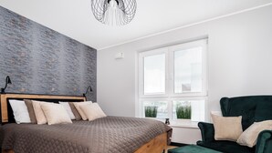 Un dormitorio moderno con una cama de madera, un sillón verde y un ventanal con persianas.