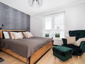 A modern bedroom with a wooden bed, a green armchair, and a large window with blinds. - Targowa Elegant Apartment (Łódź)