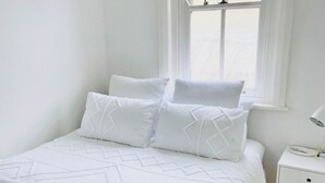 Uma cama bem arrumada com um cobre-leito estampado, uma pilha de mantas dobradas e uma mesa de cabeceira com abajur.