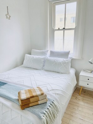 A neatly made bed with a patterned bedspread, a stack of folded blankets, and a bedside table with a lamp. - Step Out to the Seaside From Manly Beach Pad (Manly)