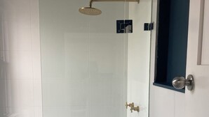 Um chuveiro com paredes de vidro, um chuveiro manual, uma porta com puxador redondo e um chão com padrão geométrico.
