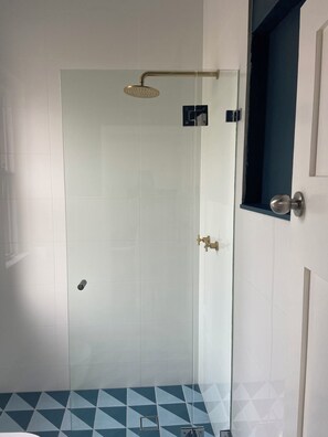 A glass-enclosed shower with a handheld showerhead, a door with a round handle, and a geometric-patterned floor. - Step Out to the Seaside From Manly Beach Pad (Manly)