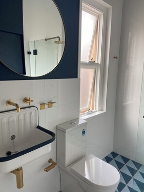 Ein Badezimmer mit weißem Waschbecken, Toilette, Spiegel und Fenster.