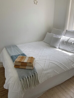 Ein ordentlich bezogenes Bett mit einer weißen Daunendecke, einer blau-beigen Streifen-Bettdecke und passendem Überwurf.