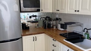 Uma cozinha com armários brancos, geladeira de aço inoxidável, micro-ondas, cafeteira e lava-louças.