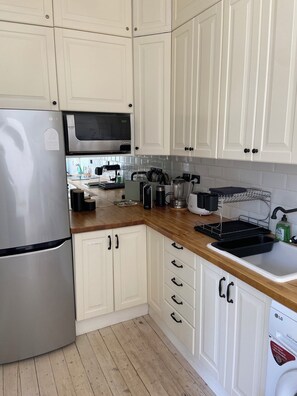 Eine Küche mit weißen Schränken, einem Edelstahl-Kühlschrank, einer Mikrowelle, einer Kaffeemaschine und einem Geschirrspüler.