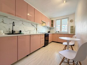 Eine moderne Küche mit rosa Schränken, einer Marmor-Spritzschutzwand und einem kleinen Essbereich mit weißem Tisch und Stühlen.