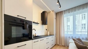 A modern kitchen with a built-in oven, a range hood, and a window with sheer curtains. - Stawowa Deluxe Apartment (Wrocław)