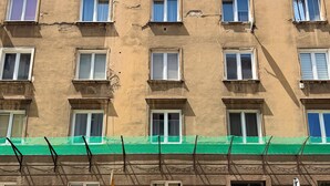 A multi-story building with numerous windows, some with curtains, and a green netting structure at the ground level. - Stawowa Deluxe Apartment (Wrocław)