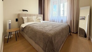 A bedroom with a bed, a bedside table, a mirror, and a window with curtains. - Stawowa Deluxe Apartment (Wrocław)