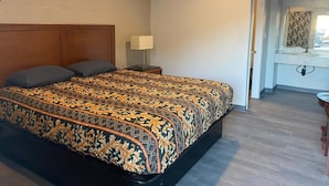 Un dormitorio con cabecera de madera, cama con ropa de cama estampada, mesita de noche con lámpara y ventana con vistas.