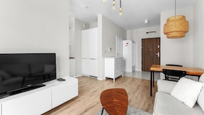 Een moderne woonkamer met een flatscreen televisie, een eethoek met een houten tafel, en een keuken op de achtergrond.
