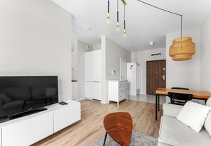 Ein modernes Wohnzimmer mit Flachbildfernseher, einem Essbereich mit Holztisch und einer Küche im Hintergrund.
