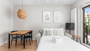 Een moderne slaapkamer met een houten eettafel, een bank, een bed met wit beddengoed en twee ingelijste foto's aan de muur.