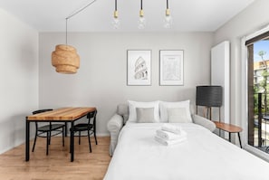 Ein modernes Schlafzimmer mit Holztisch, einer Couch, einem Bett mit weißer Bettwäsche und zwei gerahmten Bildern an der Wand.