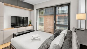 Una camera d'albergo moderna con un letto grande, una TV a schermo piatto, una porta-finestra scorrevole su un balcone e una scrivania con lampada.