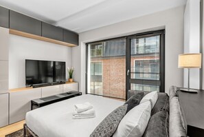A modern hotel room with a large bed, a flat-screen TV, a sliding glass door to a balcony, and a desk with a lamp. - Main Station Comfort Studio (Kraków)
